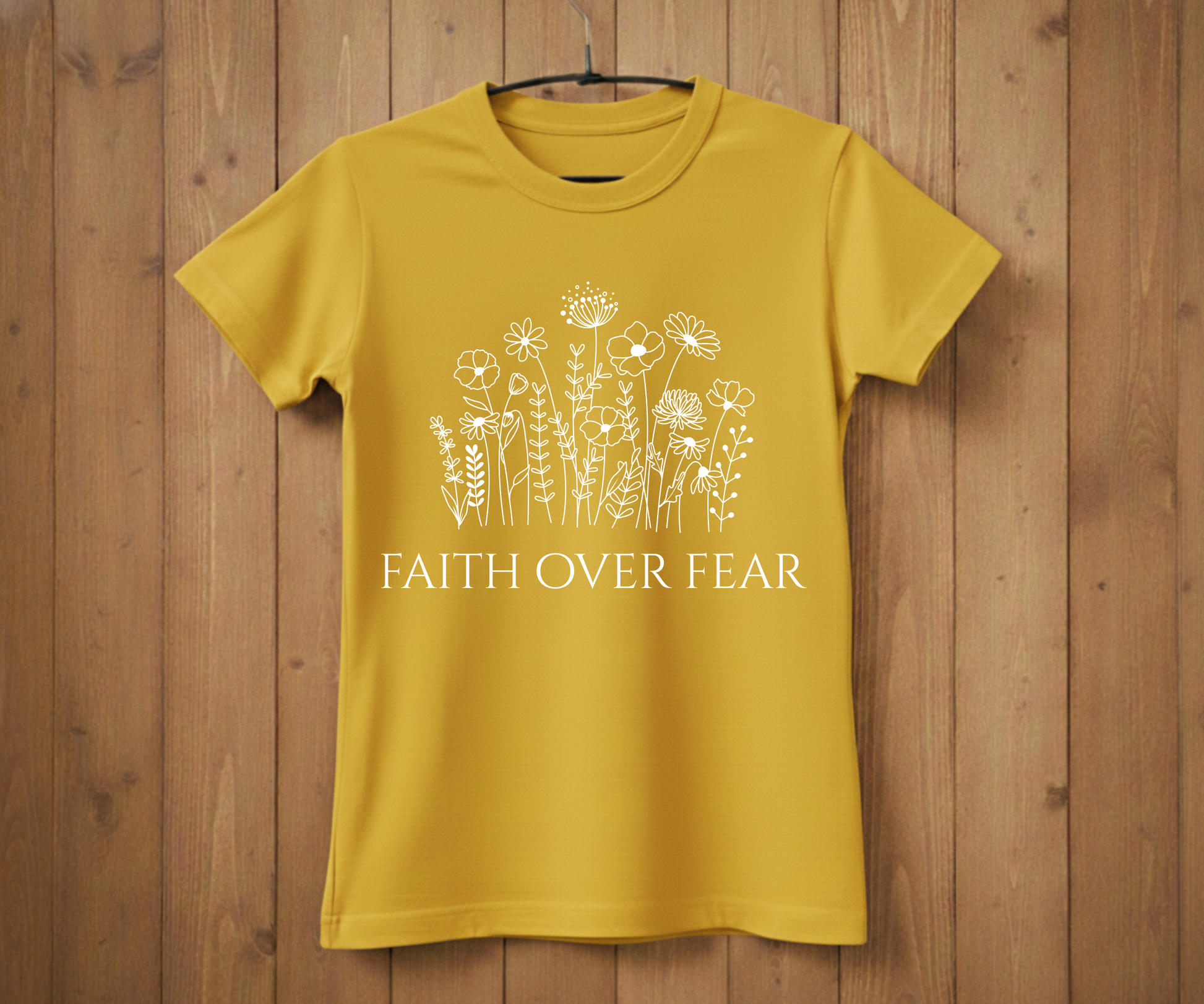 Yellow t-shirt with floral design and 'Faith Over Fear' text on a wooden background