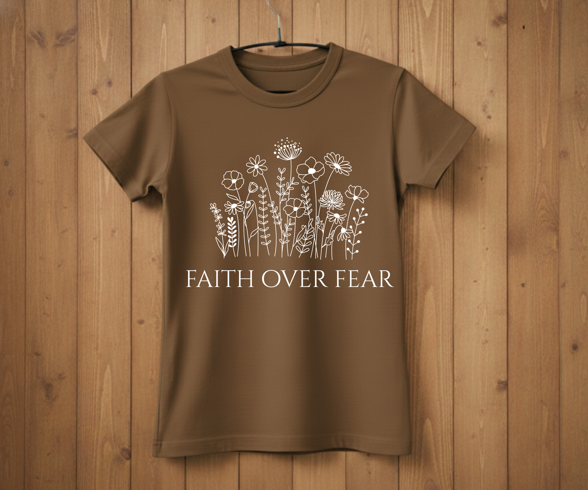 Brown t-shirt with floral design and 'Faith Over Fear' text on a wooden background