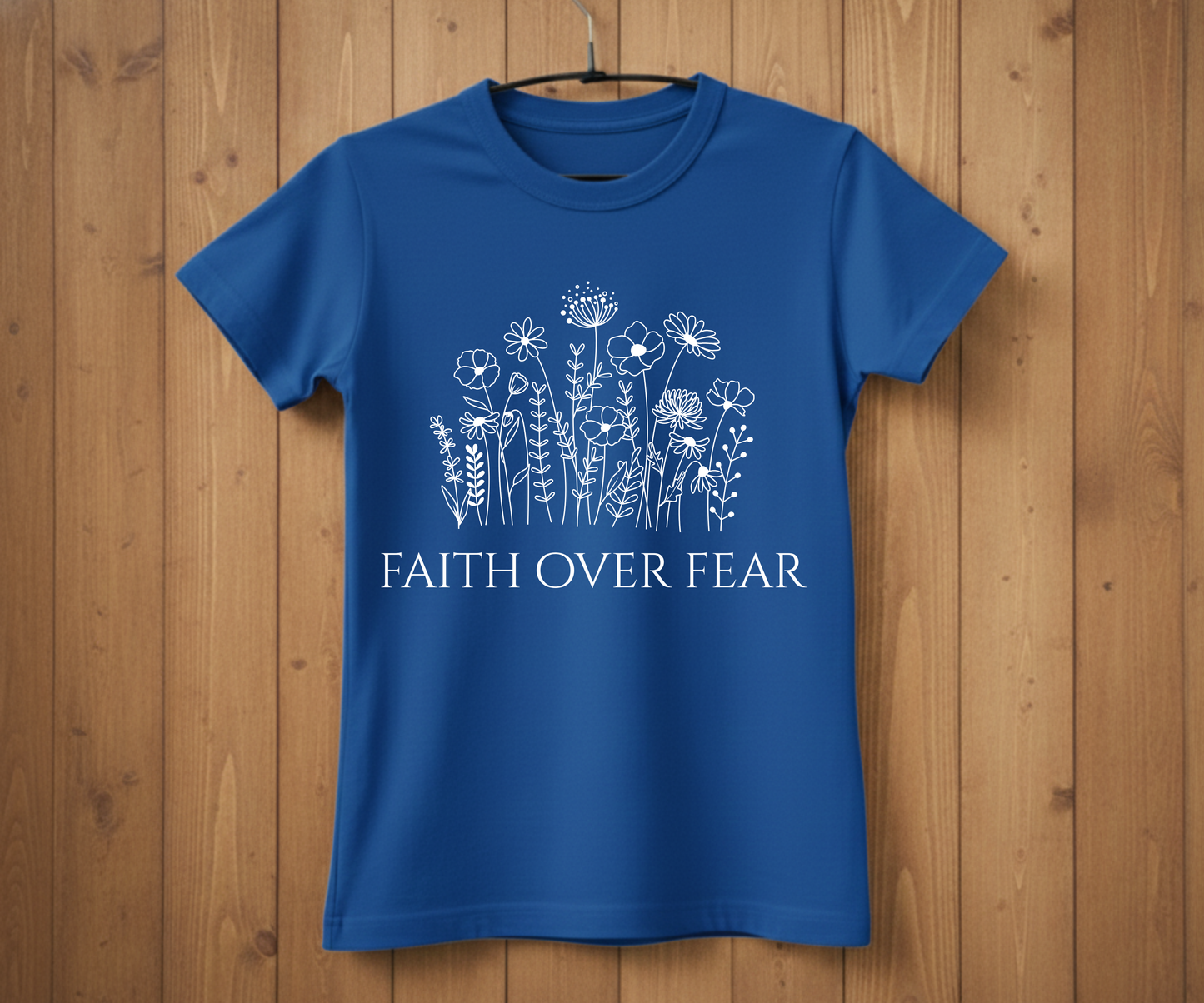 Blue t-shirt with floral design and 'Faith Over Fear' text on a wooden background