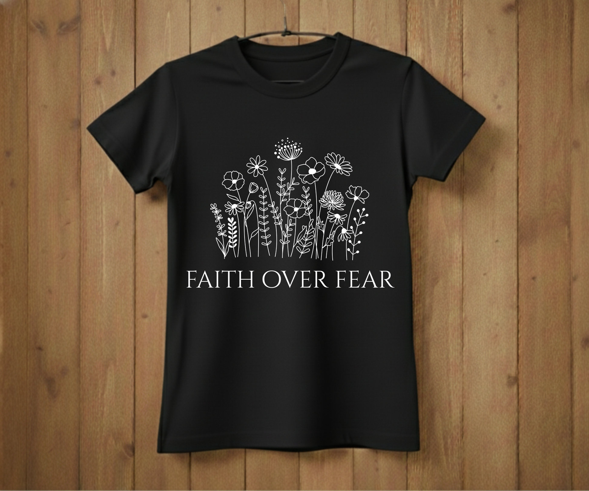 Black t-shirt with floral design and 'Faith Over Fear' text on a wooden background