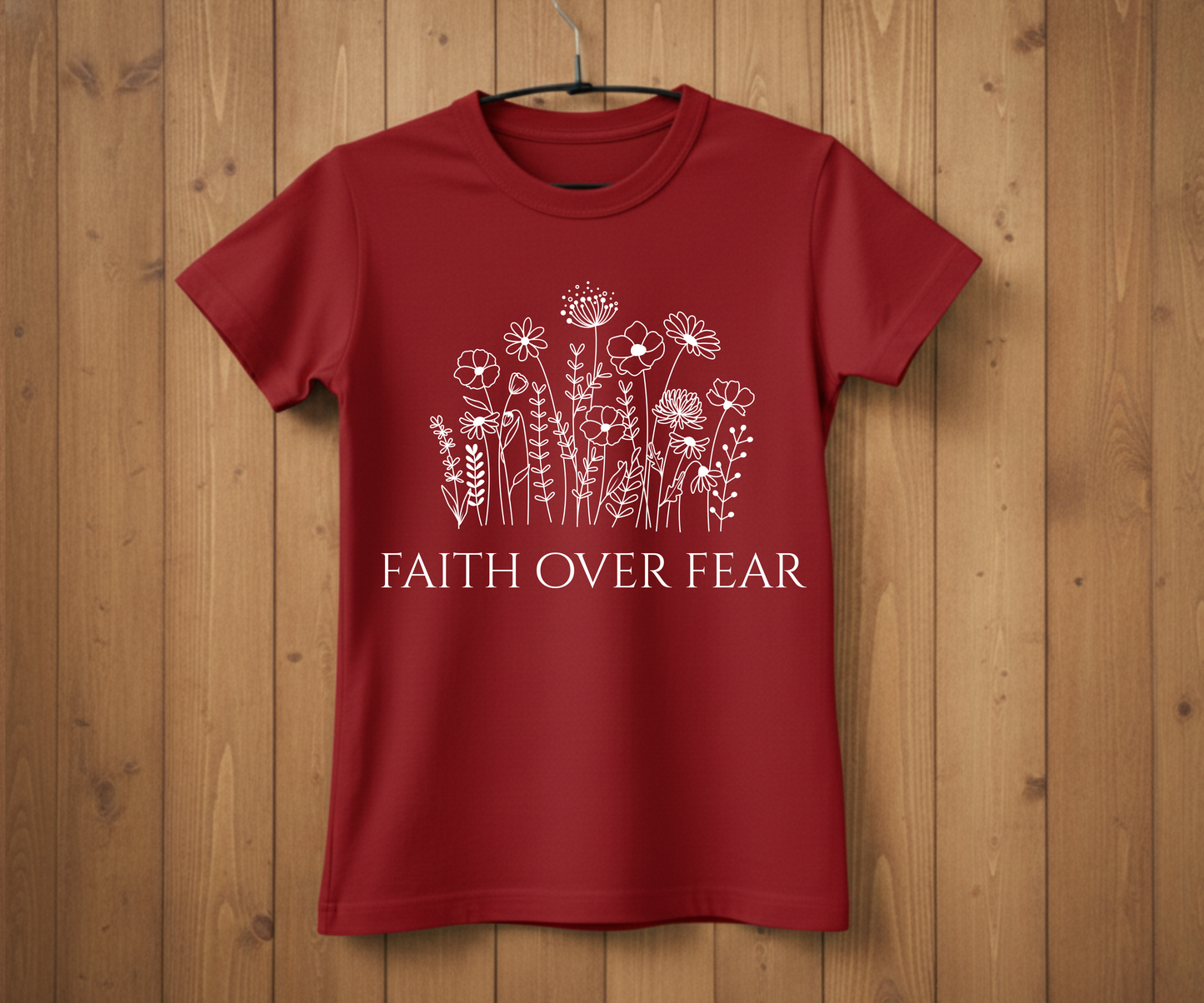 Red t-shirt with floral design and 'Faith Over Fear' text on a wooden background