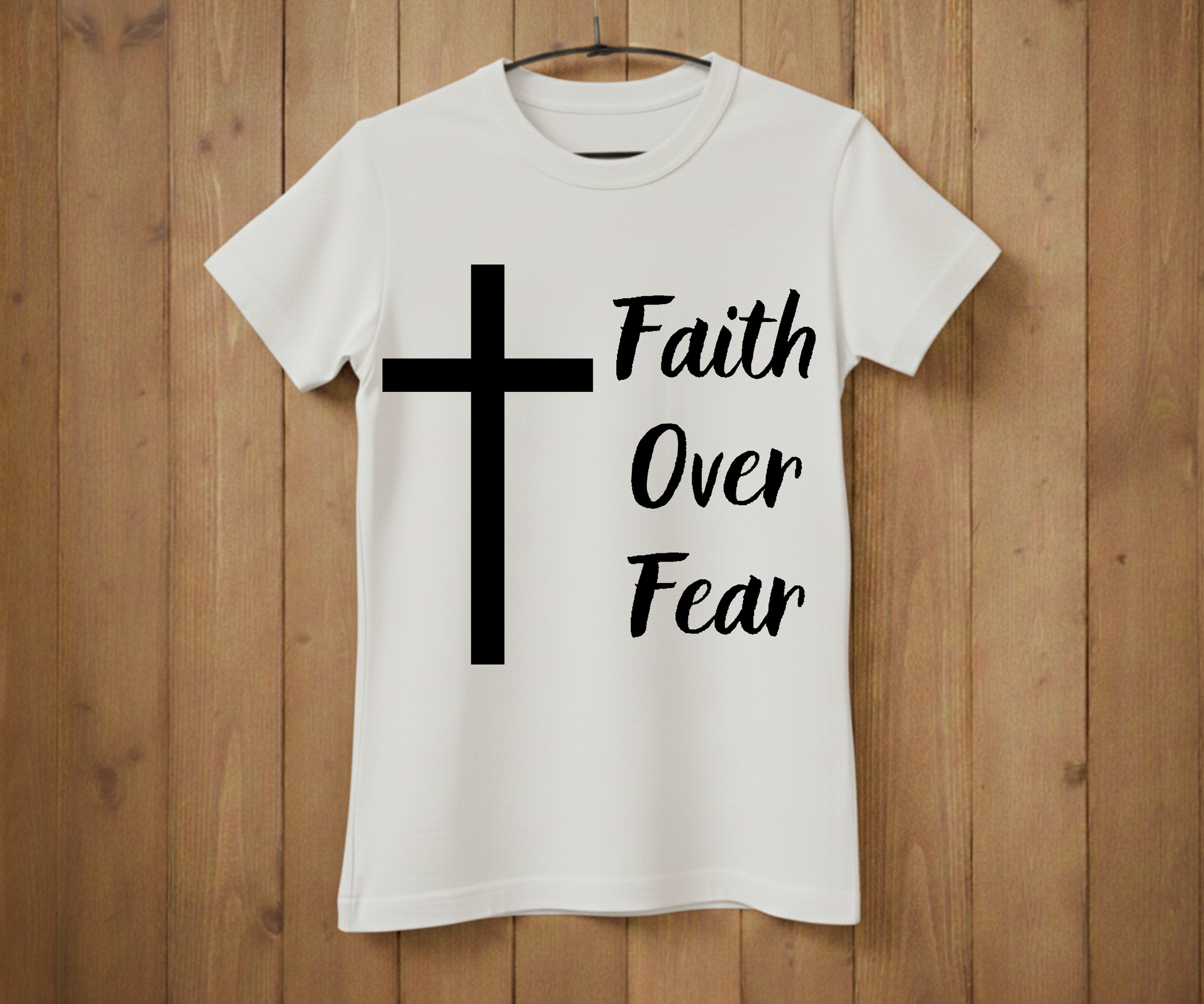 White t-shirt with a black cross and 'Faith Over Fear' text on a wooden background