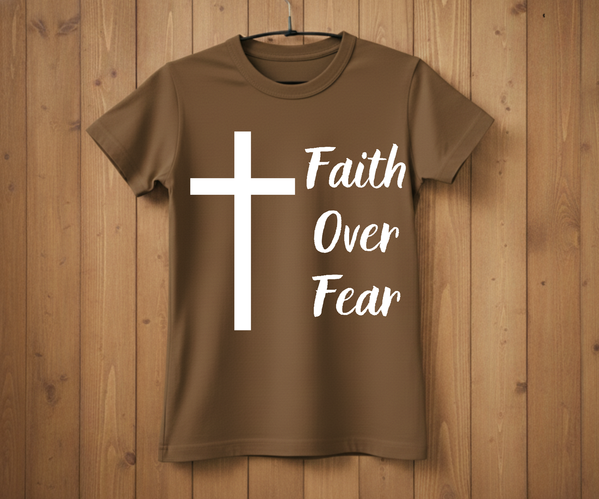 Brown t-shirt with a white cross and 'Faith Over Fear' text on a wooden background